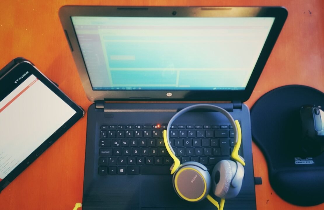 Laptop mit Tablet, Kopfhörern und Maus auf einem Tisch