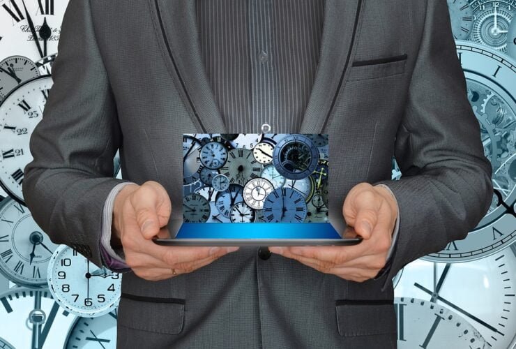 Mann im Anzug hält ein Tablet vor einem Uhrenmuster