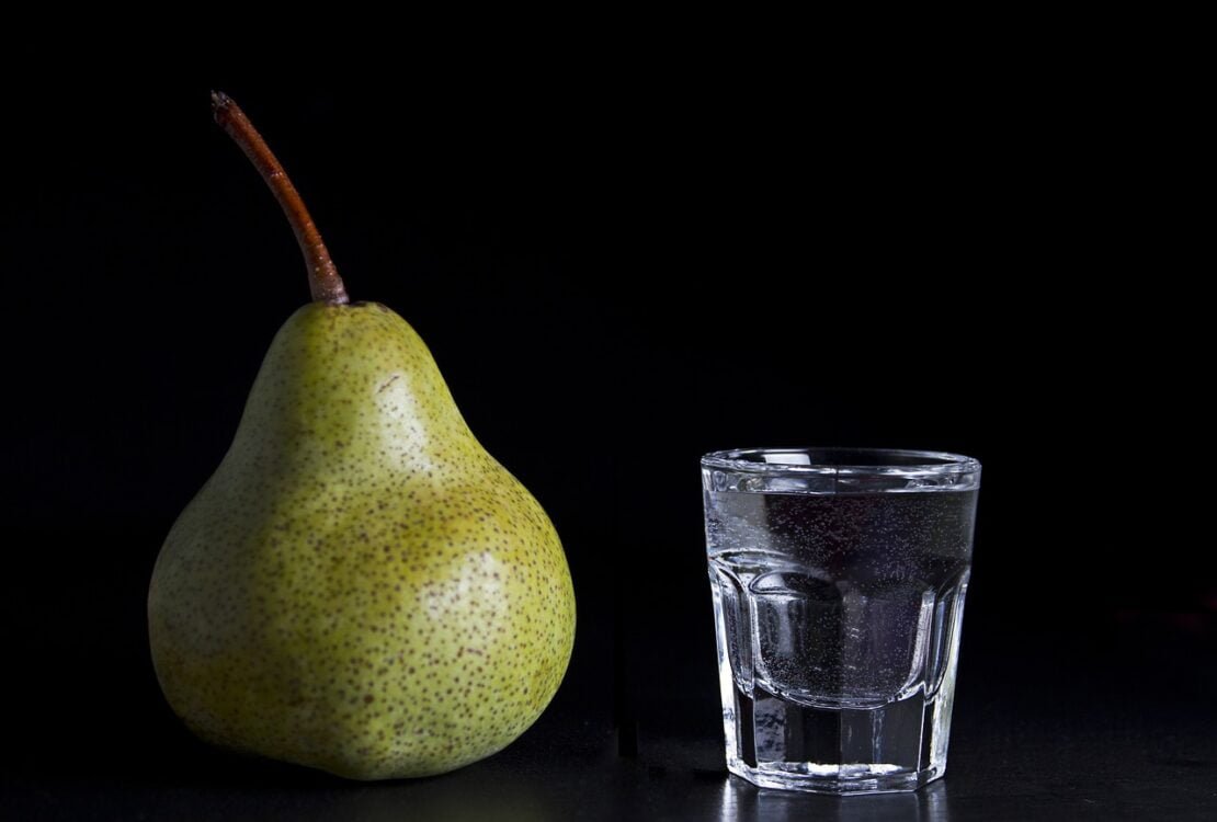 Birne neben einem Glas Wasser auf schwarzem Grund