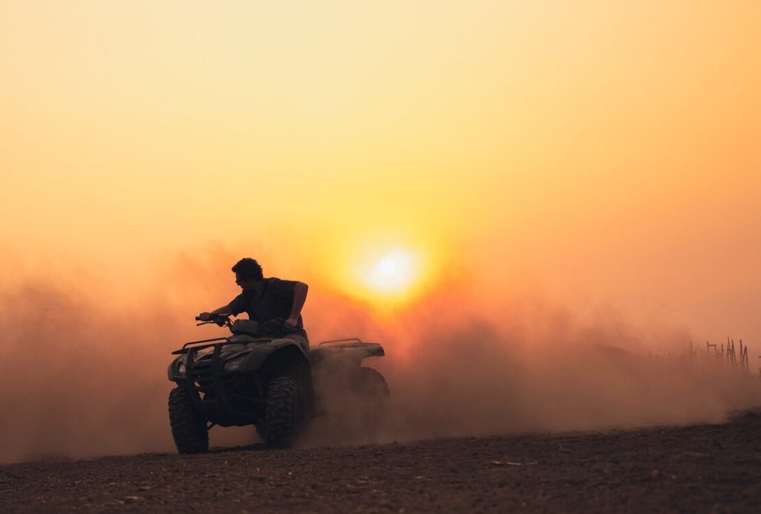 Quadfahrer fährt bei Sonnenuntergang durch Staub
