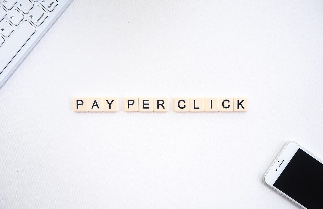 Schriftzug Pay Per Click neben Tastatur und Smartphone