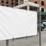 Großformatiges Werbebanner an einem Bauzaun mit sichtbaren Ösen und Kabelbindern