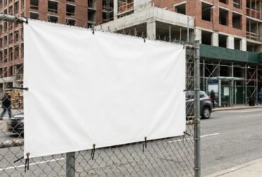Großformatiges Werbebanner an einem Bauzaun mit sichtbaren Ösen und Kabelbindern